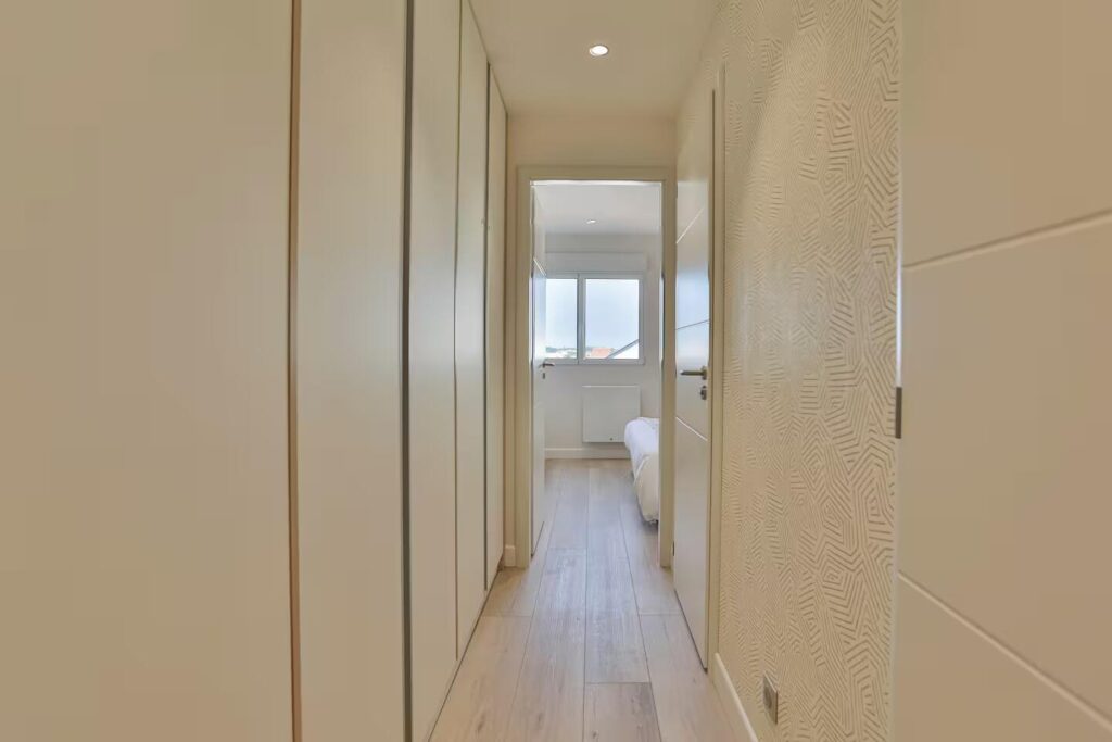 Couloir d'entrée optimisé avec de grands placards de rangement toute hauteur et papier peint graphique beige et blanc.