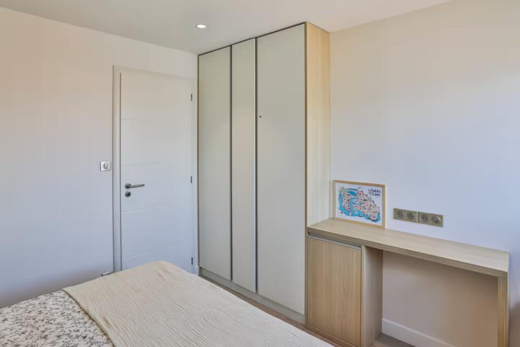 Aménagement d'un coin bureau compact intégré à un dressing toute hauteur en bois clair, idéal pour le télétravail face mer.