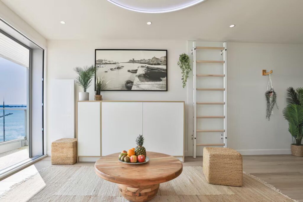 Pièce de vie lumineuse avec meuble TV blanc épuré et table basse circulaire en bois exotique, encadrant la vue sur le remblai.