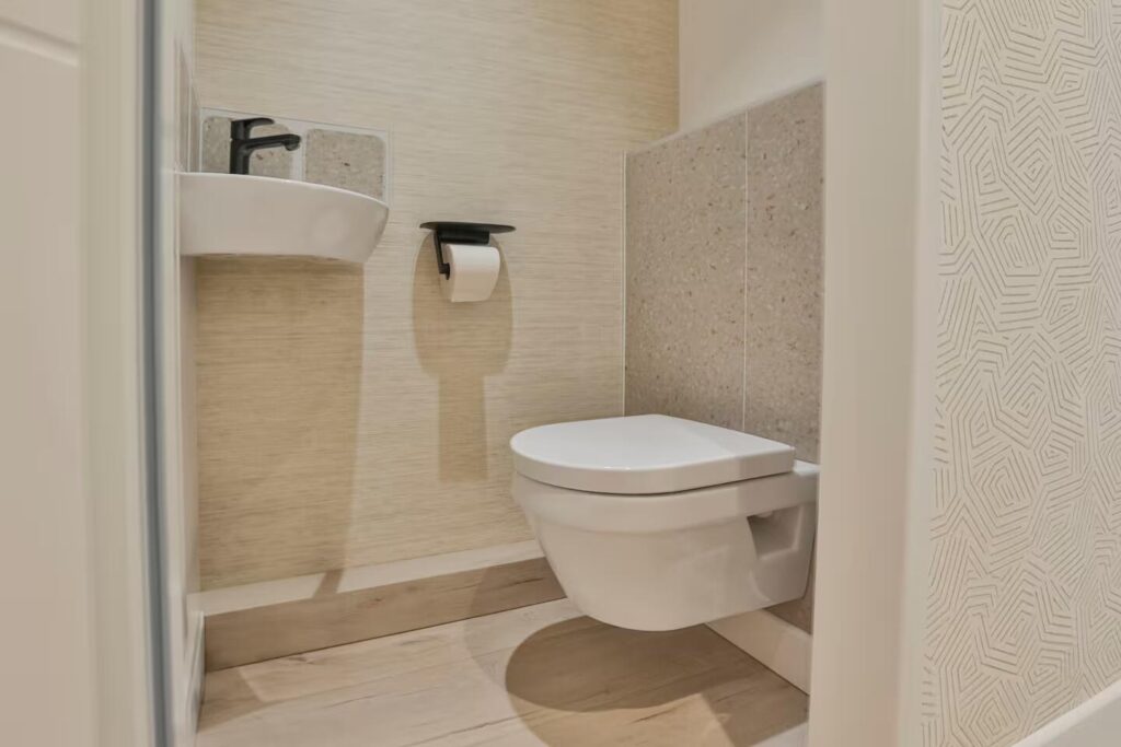 Rénovation des toilettes avec WC suspendus, carrelage terrazzo beige et papier peint aux motifs géométriques fins.