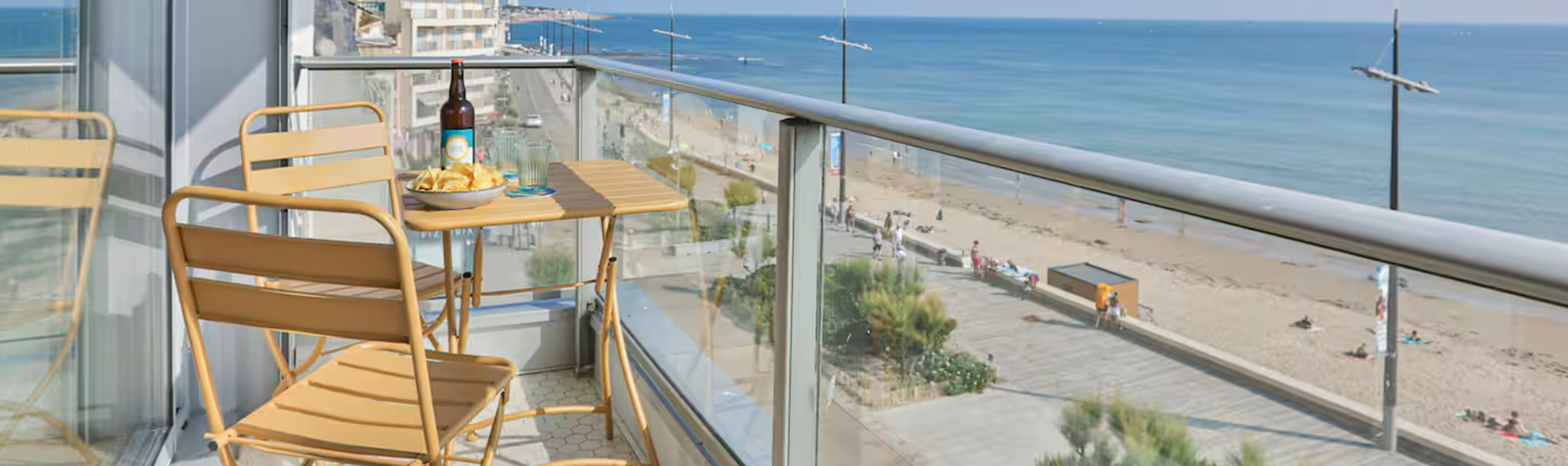 Balcon avec vue panoramique sur la plage des Sables-d'Olonne, aménagé avec du mobilier de terrasse ocre en harmonie avec le soleil couchant.
