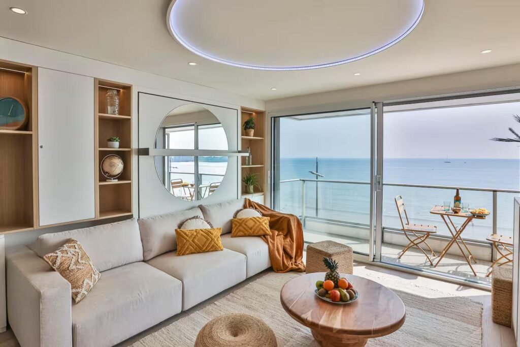 Salon contemporain avec canapé crème, table basse en bois massif et grande baie vitrée ouvrant sur l'océan aux Sables-d'Olonne.