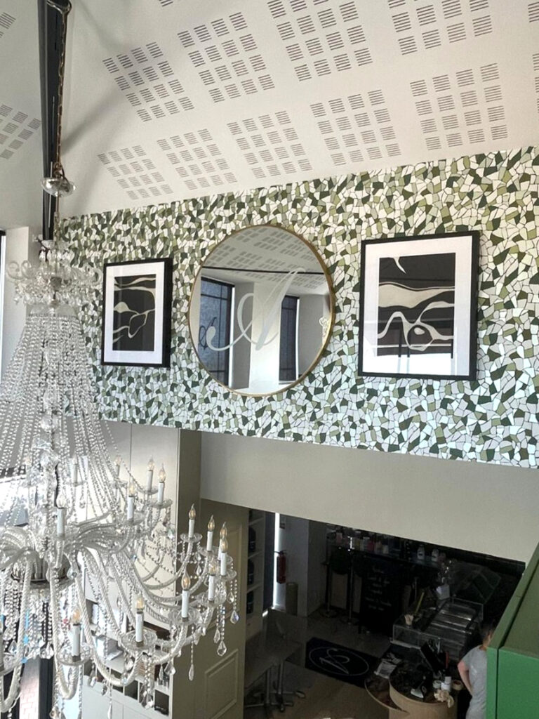 Architecture intérieure du salon de thé Amanda avec un lustre monumental en cristal, une mezzanine élégante et un mur décoratif en mosaïque de papier peint vert et blanc.