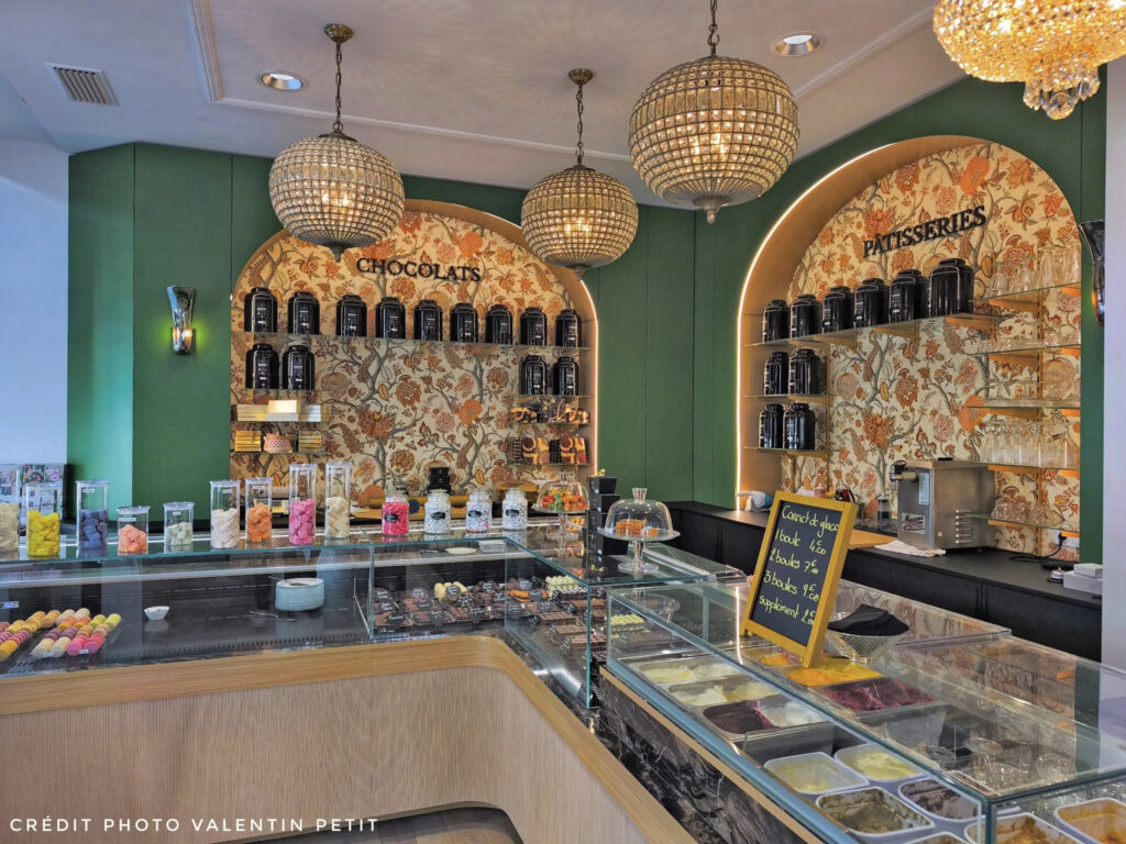 Rayonnages de vente avec papier peint fleuri Pierre Frey, bocaux de confiseries colorées et éclairage par suspensions boules en cristal ciselé.