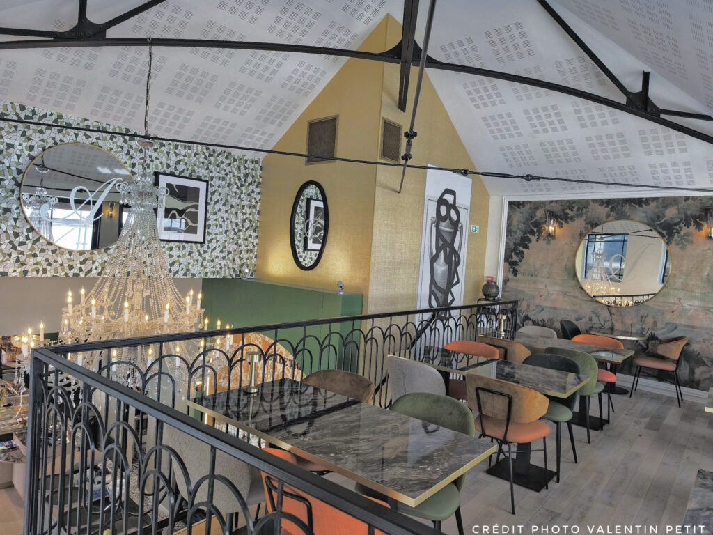 Architecture intérieure du salon de thé Amanda avec un lustre monumental en cristal, une mezzanine élégante et un mur décoratif en mosaïque de papier peint vert et blanc.