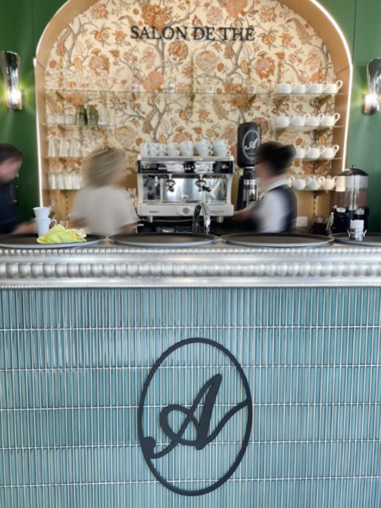 Détail du bar avec revêtement en mosaïque bleue verticale, logo "A" en métal noir et plateau en étain massif confectionné par les Ateliers Nectoux.