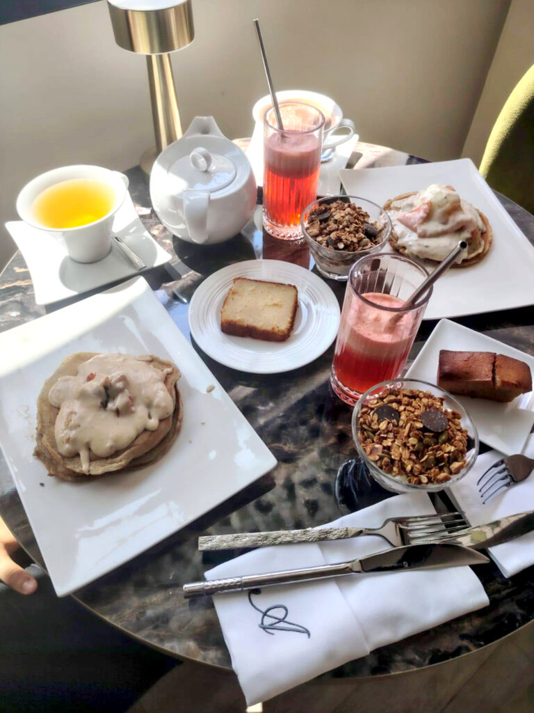 Art de la table au salon de thé Amanda : pancakes gourmands, jus de fruits frais et thé servis sur des tables en marbre avec serviettes brodées au logo de l'institution.
