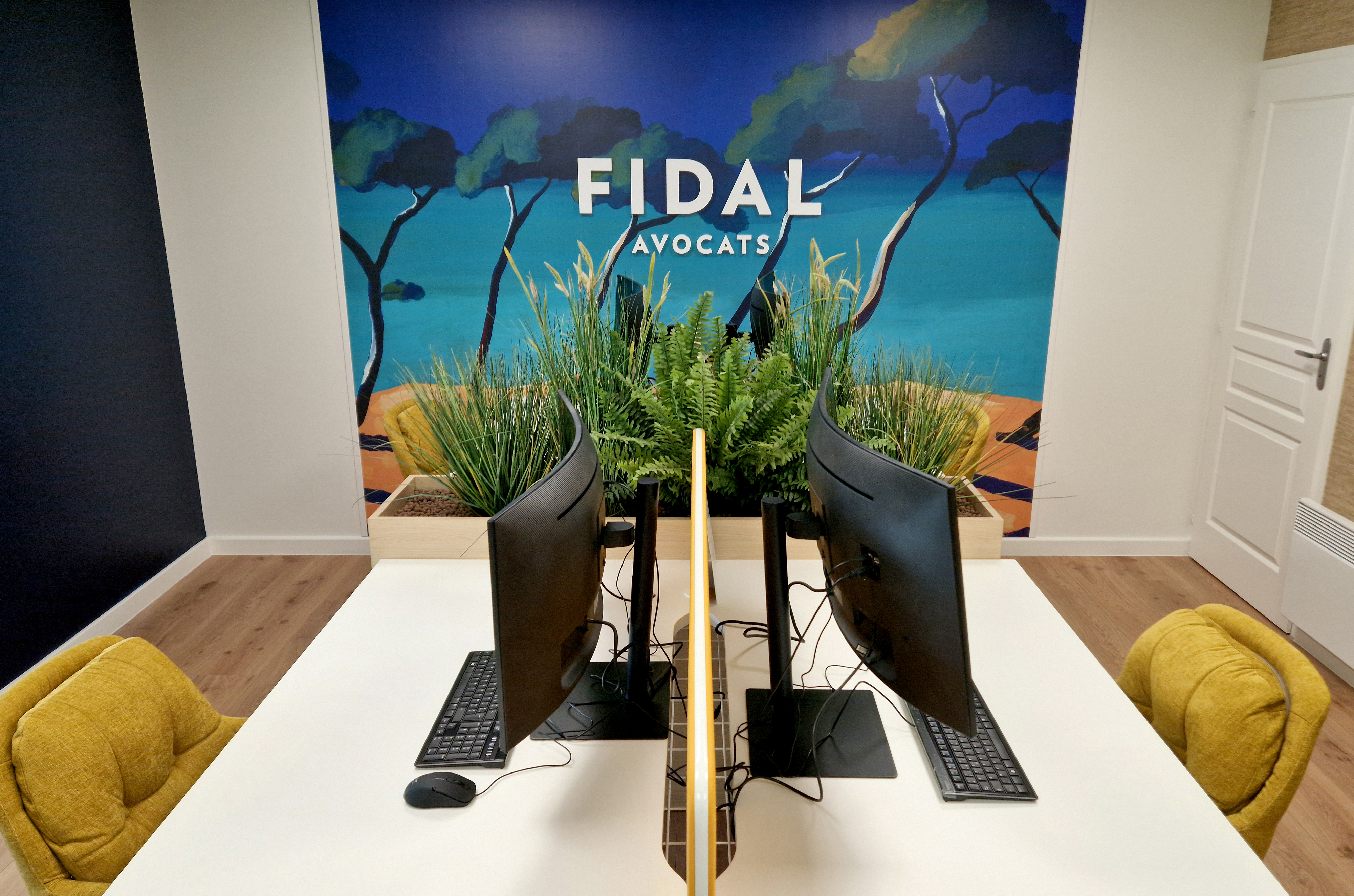 Aménagement d'un bureau paysager par Studio Vesta pour le cabinet Fidal, incluant des postes de travail blancs avec écrans acoustiques jaunes et une fresque murale panoramique représentant une vue côtière.