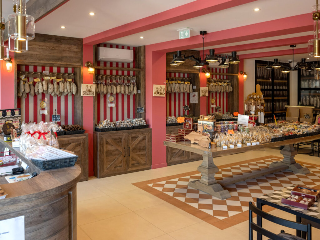 Aménagement intérieur d'une boutique de charcuterie par Studio Vesta, avec un sol en damier terracotta, des meubles en bois brut et des murs à rayures rouges évoquant les boucheries traditionnelles.