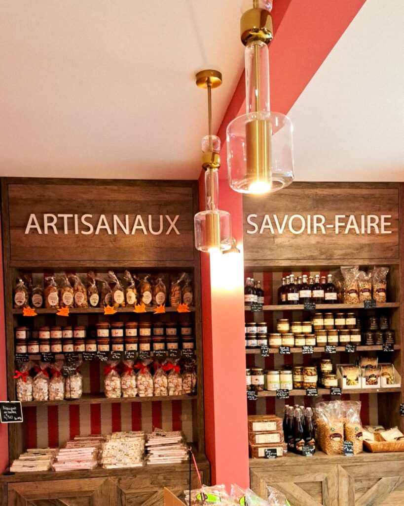 Rayonnages muraux rétroéclairés dédiés aux produits d'épicerie fine, surplombés par la mention "SAVOIR-FAIRE" en lettres blanches sur bois.