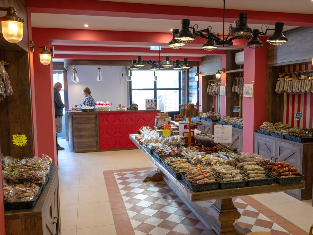 Aménagement intérieur d'une boutique de charcuterie par Studio Vesta, avec un sol en damier terracotta, des meubles en bois brut et des murs à rayures rouges évoquant les boucheries traditionnelles.