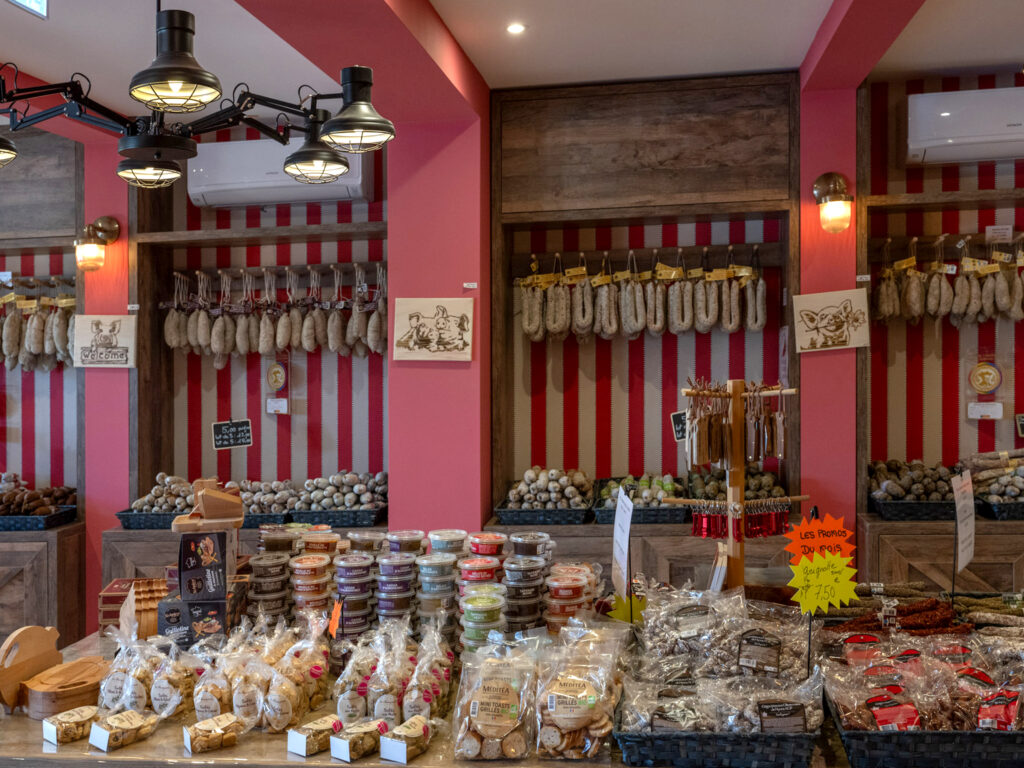 Rayonnages sur mesure en bois avec fond à rayures rouges et blanches, présentant une gamme de saucissons artisanaux suspendus et en paniers.