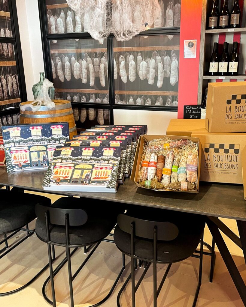 Présentation de coffrets cadeaux et calendriers de l'Avent sur une table en métal noir, avec vue sur l'espace séchoir vitré en arrière-plan.