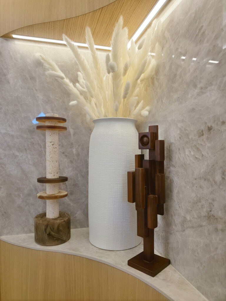 Composition décorative dans une niche courbe avec vase blanc texturé, herbes de pampa et objets d'art minéraux.
