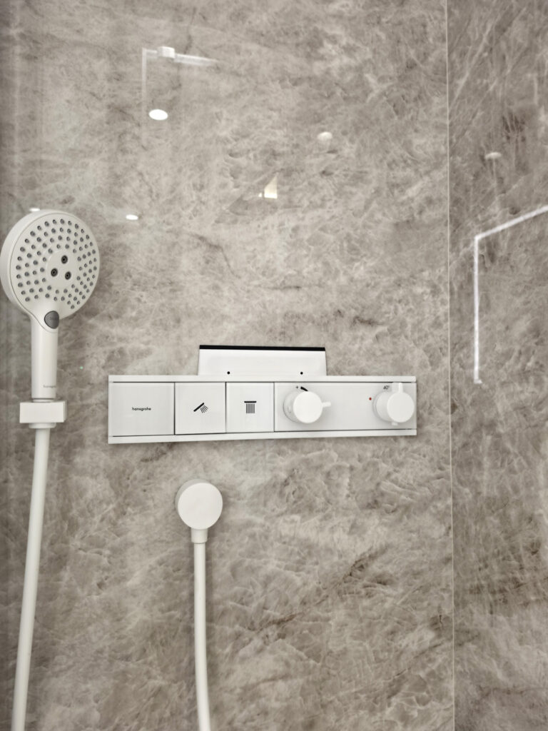 Robinetterie de douche encastrée thermostatique blanche thermostatique Hansgrohe sur carrelage effet marbre clair.