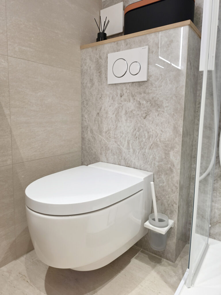 WC suspendu compact japonais avec plaque de commande double touche blanche encastrée dans un mur carrelé effet marbre.