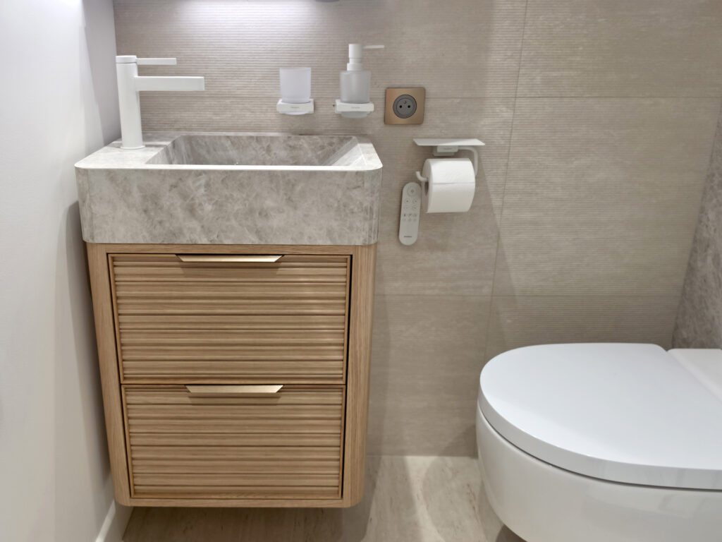Vue de face d'un meuble vasque compact en bois strié et marbre à côté d'un WC lavant avec télécommande murale.