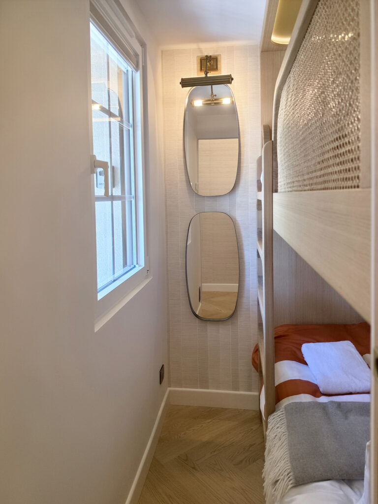 Niche étroite de chambre avec deux miroirs ovales superposés et applique en laiton rétro, rénovation d'appartement compact.