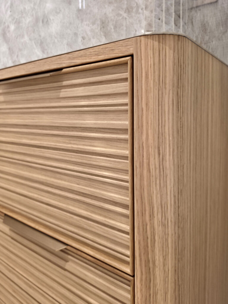 Détail d'un meuble vasque suspendu en bois strié avec angles arrondis et plan en marbre gris par Studio Vesta.