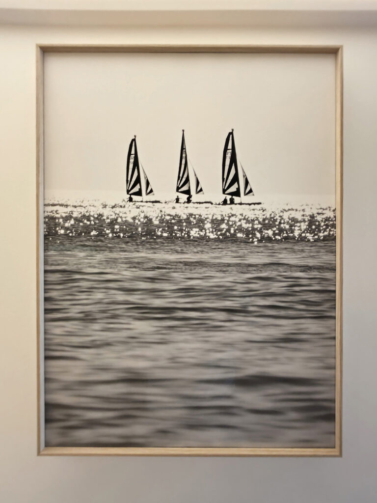 Cadre en bois clair exposant une photographie d'art en noir et blanc de voiliers en mer par Yann Lecomte.