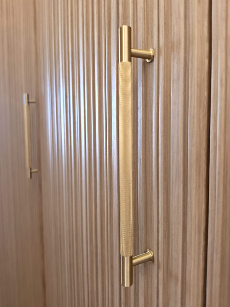 Gros plan sur une poignée de tirage moletée en laiton doré fixée sur une porte de placard en bois strié.