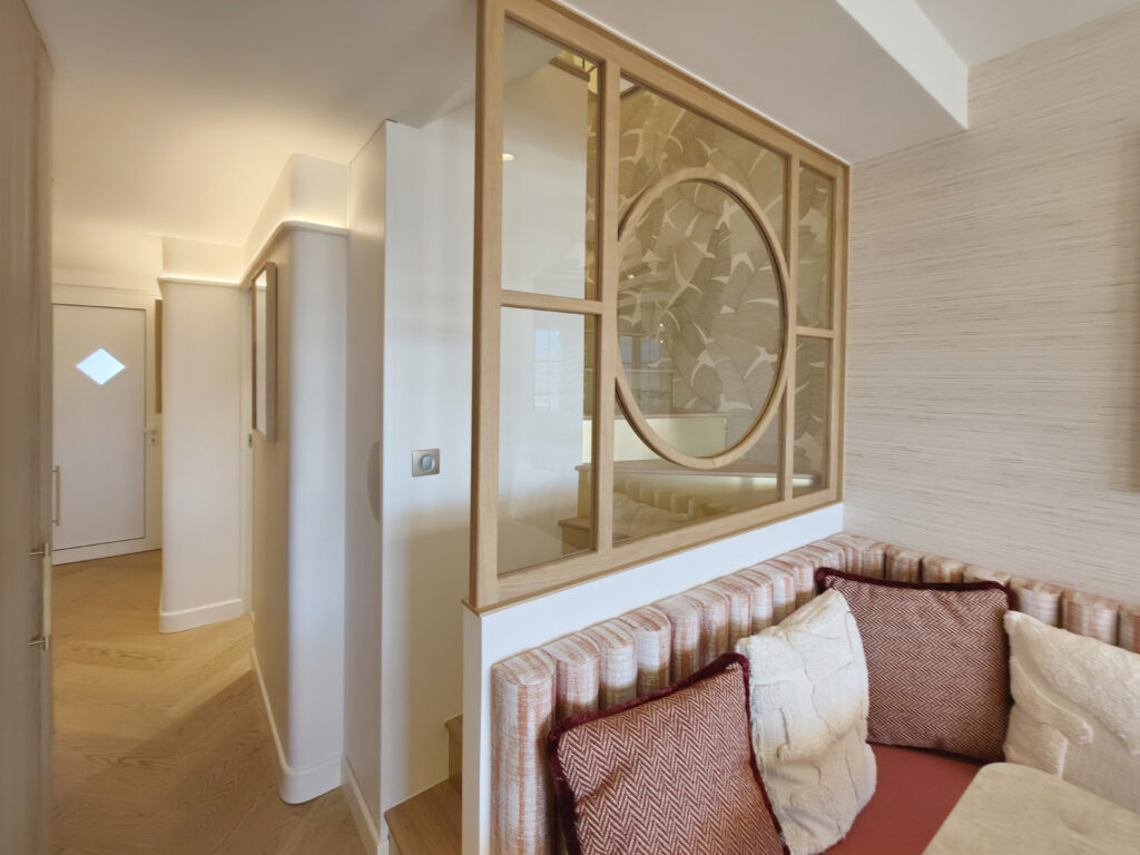 Verrière sur mesure en chêne avec motif géométrique circulaire séparant l'escalier du dossier de la banquette repas.