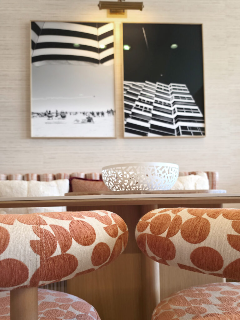 Zoom sur les dossiers arrondis de chaises en tissu à motifs géométriques corail devant deux photographies d'art encadrées.