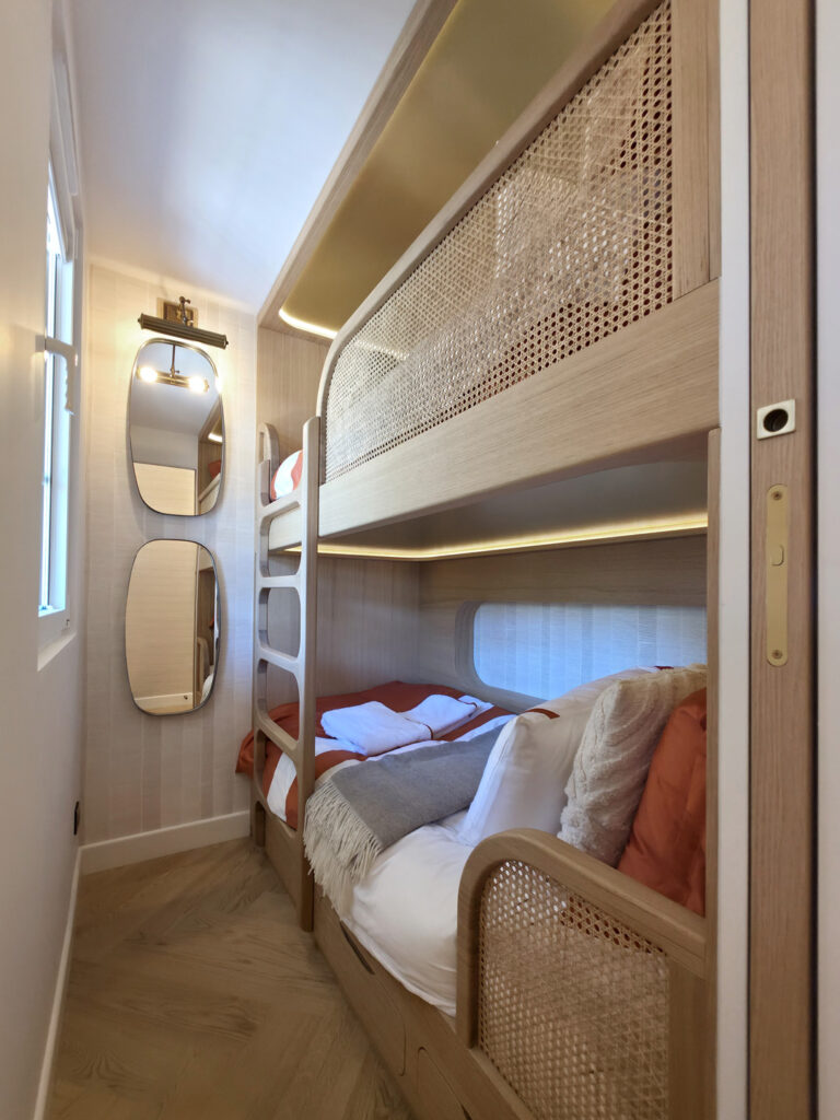 Aménagement sur mesure d'un espace dortoir compact avec lits superposés en bois et cannage, éclairage LED intégré et miroirs organiques par Studio Vesta.