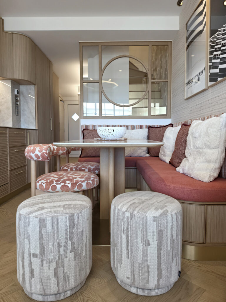 Espace repas sur mesure vu de face avec banquette sur socle en laiton, poufs bouclette, table marbre et verrière en bois clair.