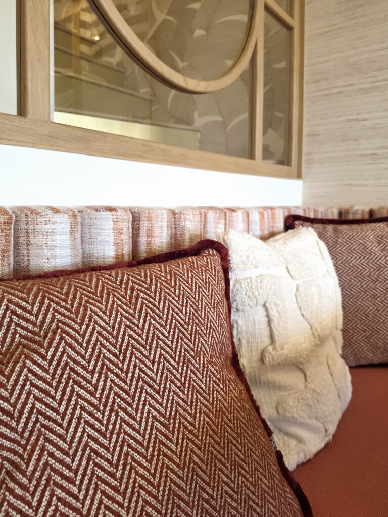 Détail de coussins en velours terracotta à motifs chevrons et maille bouclette crème posés sur la banquette repas.
