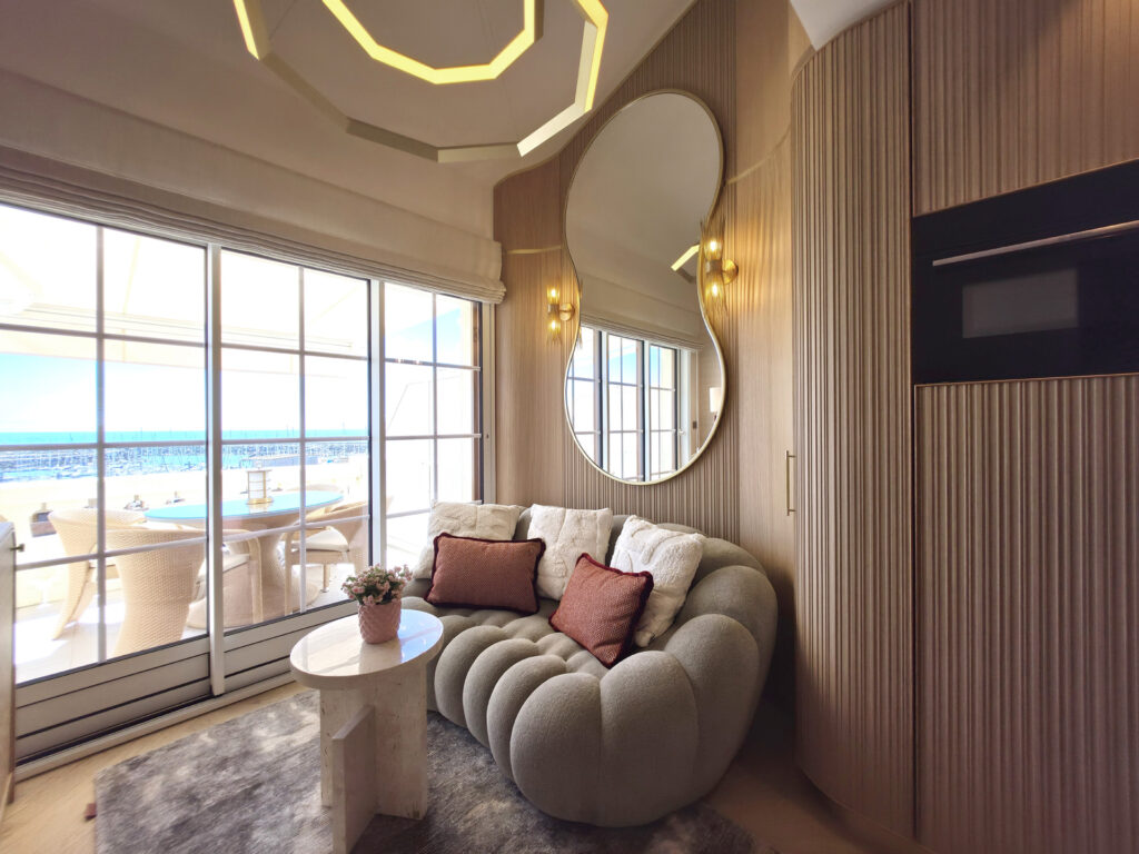 Coin salon sur mesure face à la baie vitrée donnant sur la terrasse et le port de Bourgenay, avec canapé capitonné et grand miroir sur mur strié.