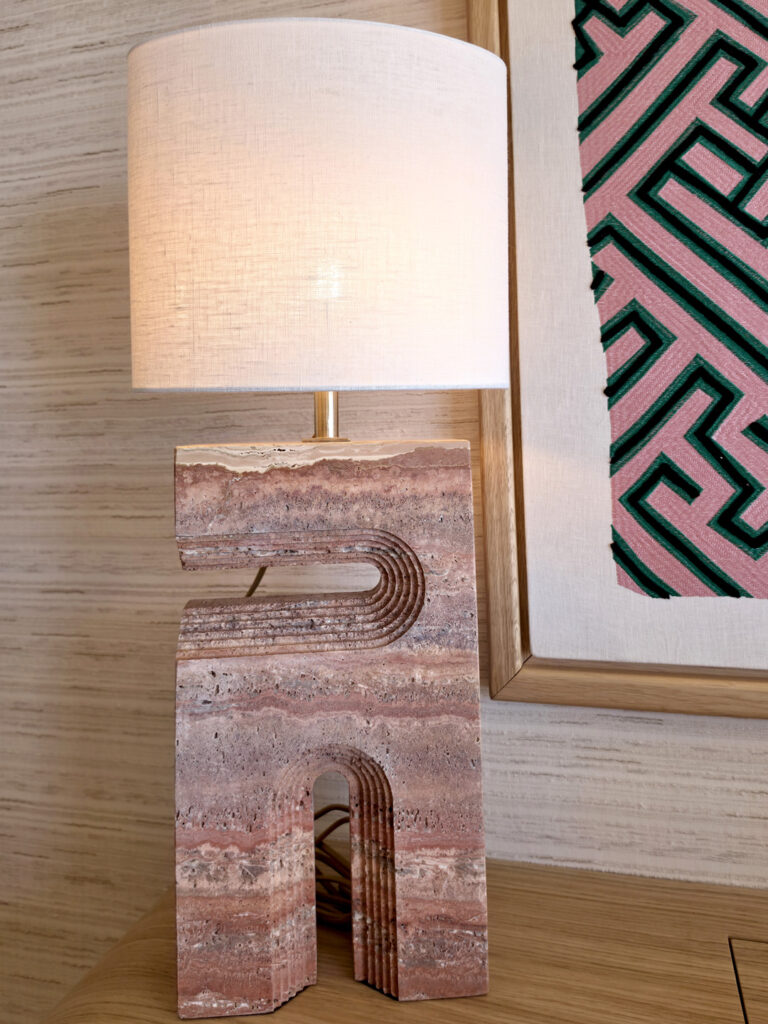 Zoom sur le pied d'une lampe à poser sculptée dans du travertin veiné avec abat-jour en lin beige.