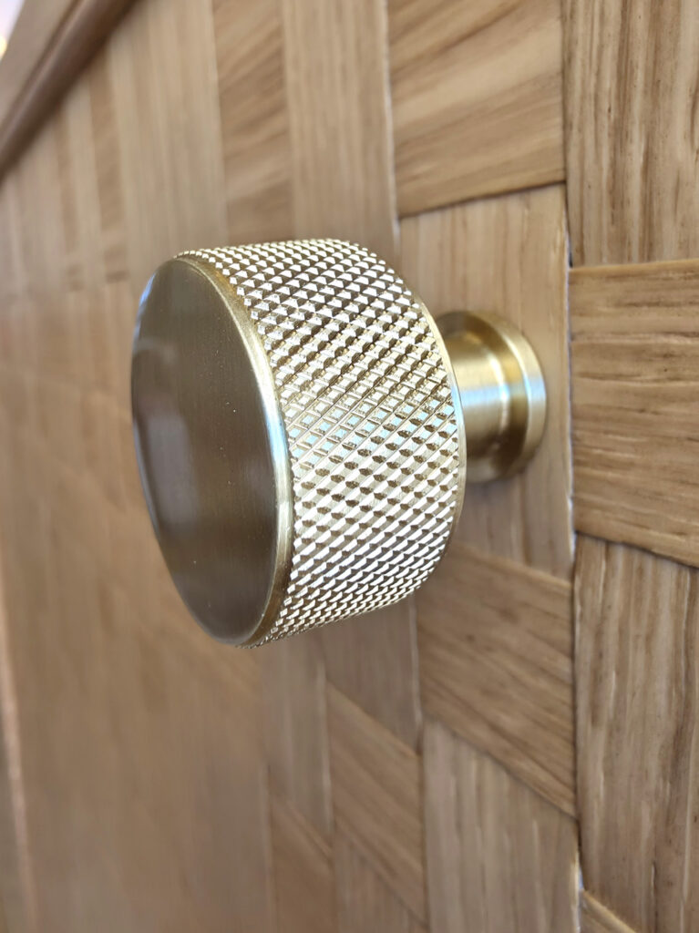 Bouton de meuble circulaire moleté en laiton doré brossé fixé sur une porte en bois tressé sur mesure.