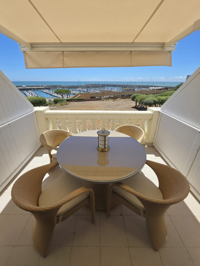 Vue imprenable sur le port de Bourgenay et l'océan depuis la terrasse aménagée d'une table ronde et quatre fauteuils tressés.