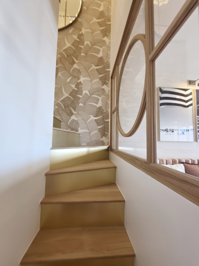 Escalier hélicoïdal sur mesure avec marches en bois clair, contre-marches en laiton doré et papier peint motif palmes.