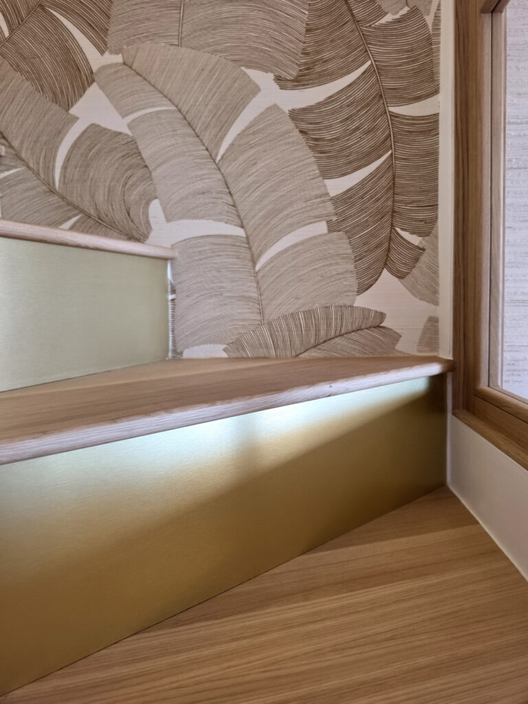 Détail d'une marche d'escalier en chêne clair avec nez de marche rétroéclairé par LED et contre-marche en laiton doré.