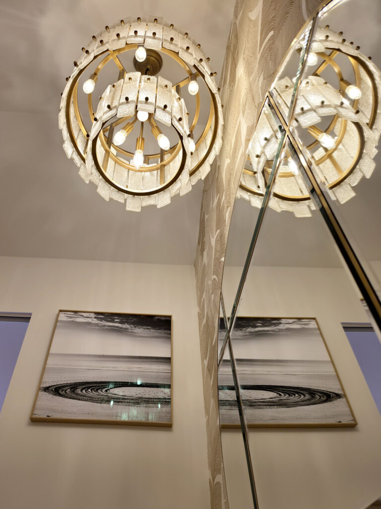 Contre-plongée sur le lustre en verre rétroéclairé et son reflet dans le miroir circulaire de la cage d'escalier.