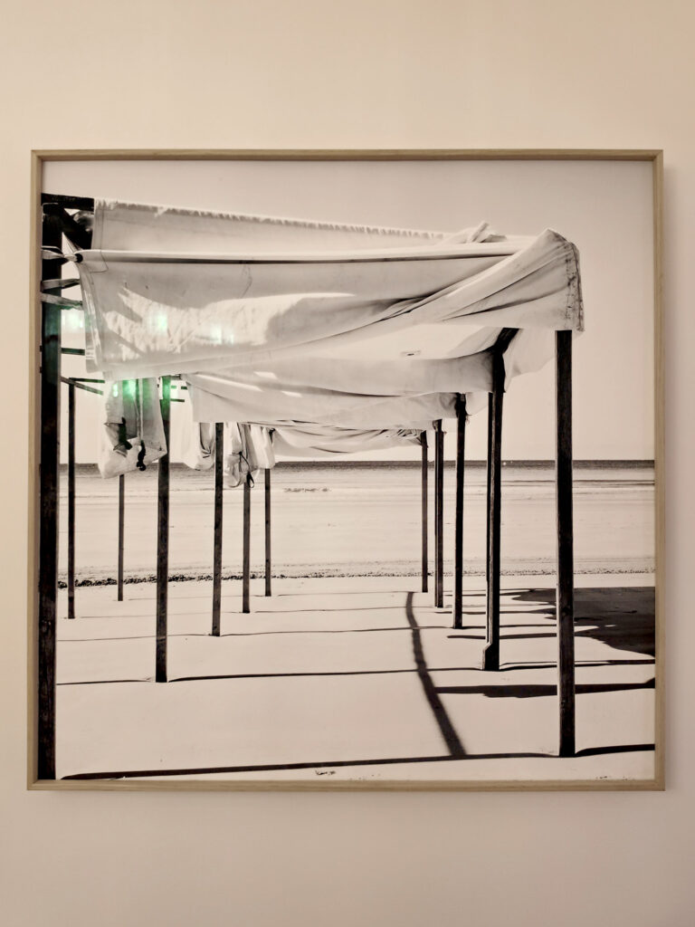 Tableau d'art encadré en bois clair montrant des structures de tentes de plage en noir et blanc par le photographe Yann Lecomte.