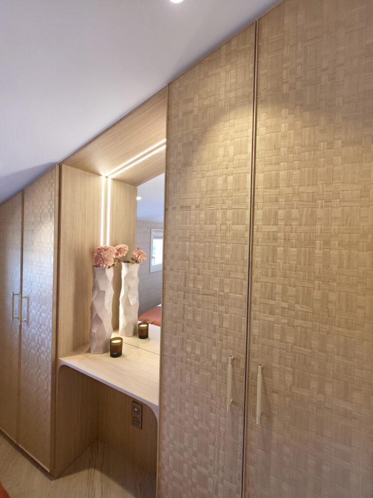 Dressing sur mesure sous pente aux façades en bois tressé avec niche coiffeuse centrale miroir et ruban LED intégré par Studio Vesta.