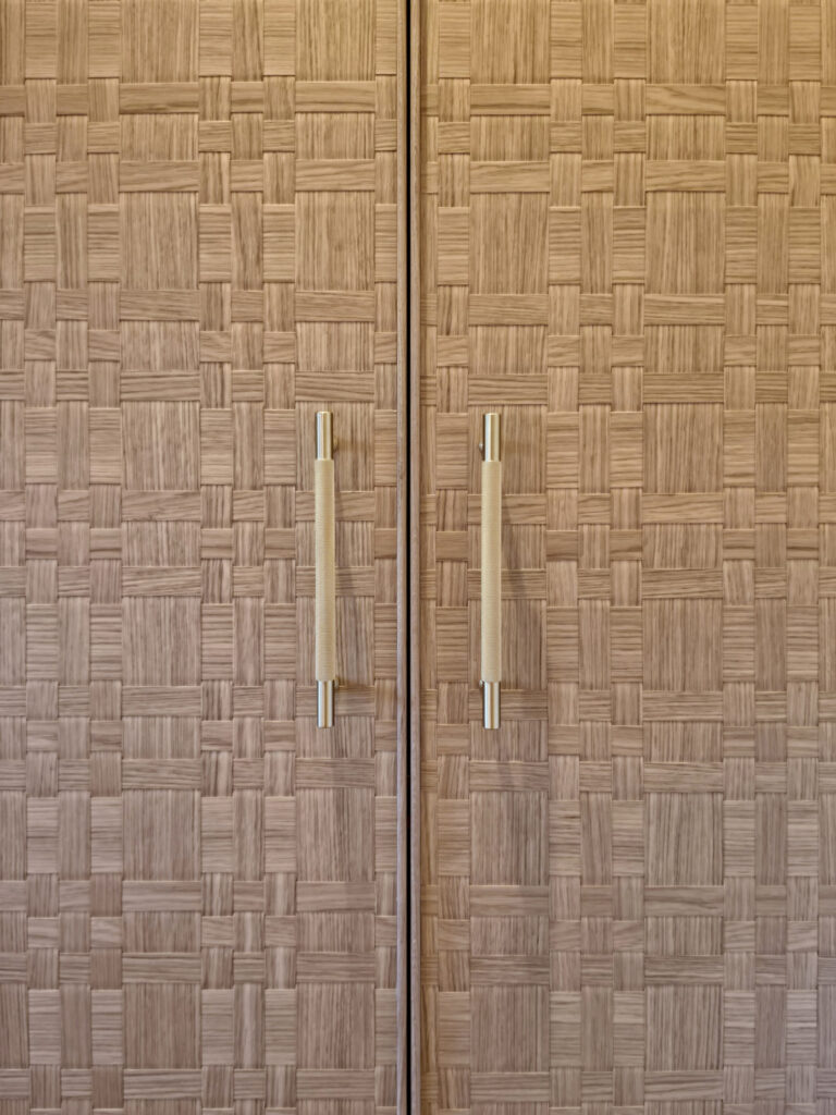 Zoom sur les panneaux de portes de placard en bois tressé et poignées moletées en laiton brossé dans la chambre parentale.