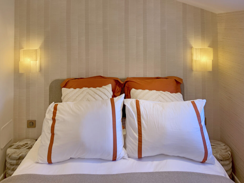 Lit coffre ultra confort avec linge de lit blanc et terracotta, appliques murales lumineuses et chevets ronds en marbre naturel.