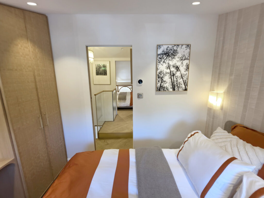 Vue depuis le lit de la chambre parentale vers le dressing tressé, la porte coulissante et le palier de l'étage.