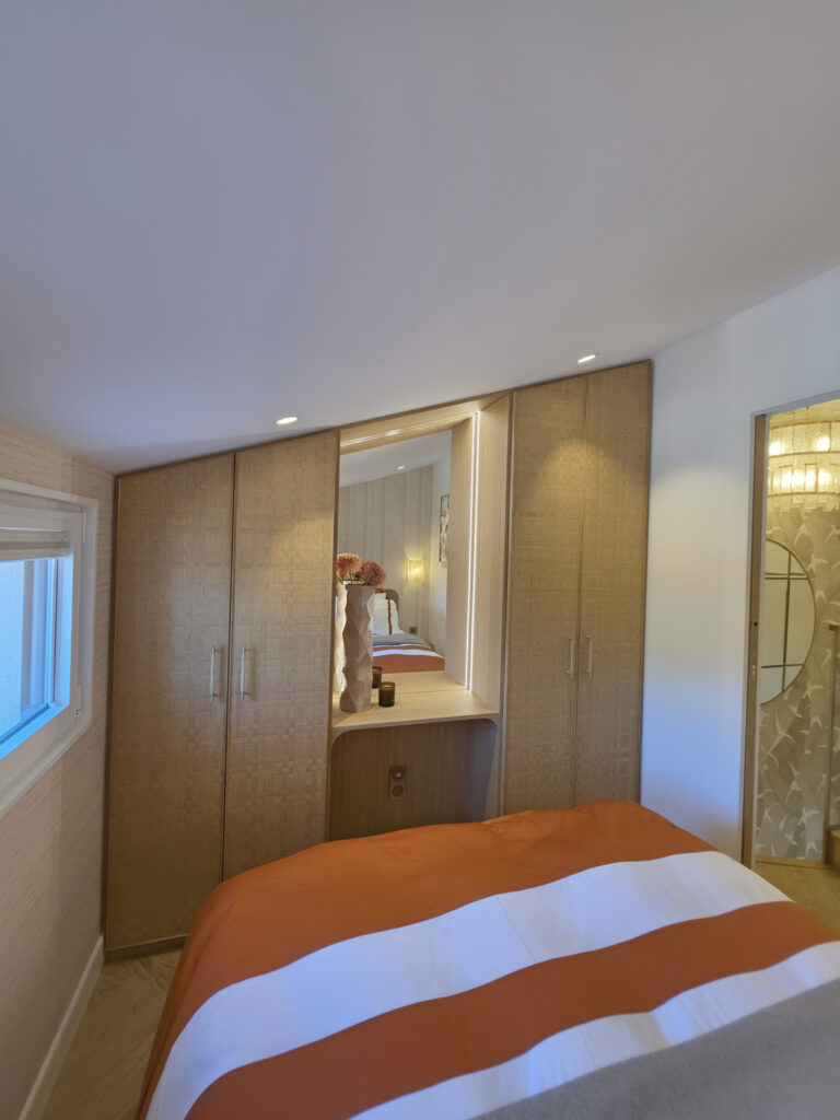 Vue globale de la chambre parentale sous pente avec grand dressing sur mesure, miroir central et lit au premier plan.