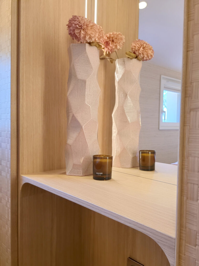 Espace coiffeuse avec tablette sur mesure en chêne clair, miroir mural, bougies parfumées Meraki et vases géométriques blancs.