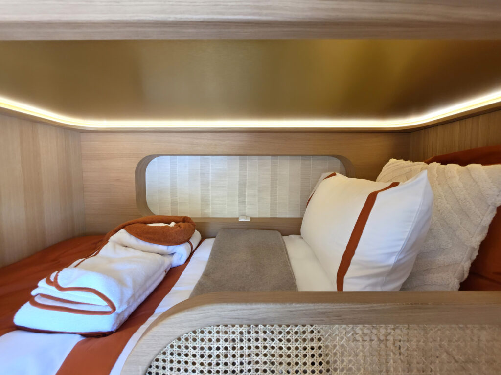 Aménagement de couchette sur mesure avec linge de maison brodé, alcôve de chevet encastrée et rétroéclairage LED.