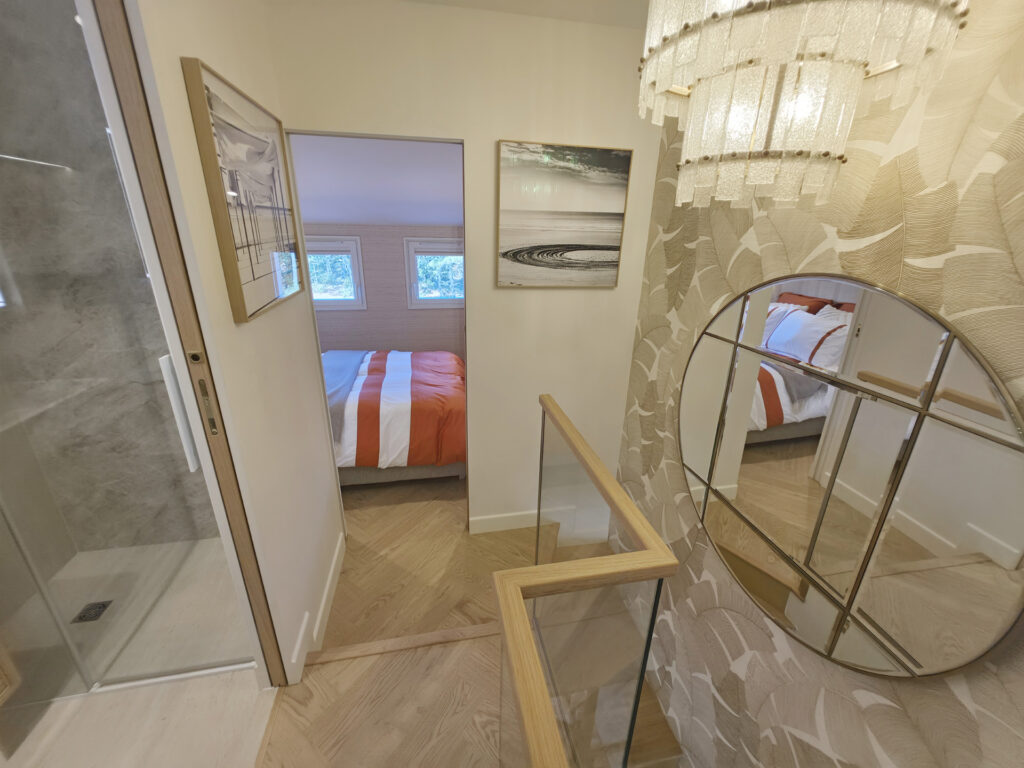 Vue depuis l'escalier vers le palier du R+1 dessert la salle d'eau à gauche, la chambre parentale en face et le miroir circulaire à droite.
