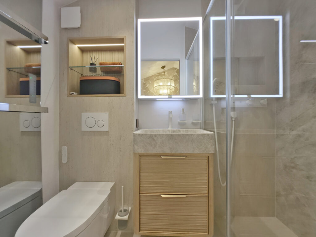 Salle d'eau compacte complète avec WC lavant suspendu, meuble vasque en chêne strié et marbre, miroir rétroéclairé et douche vitrée.