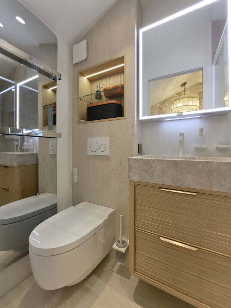 Vue trois-quarts de la salle d'eau sous pente montrant le WC suspendu japonais, la niche murale éclairée et le meuble vasque sur mesure