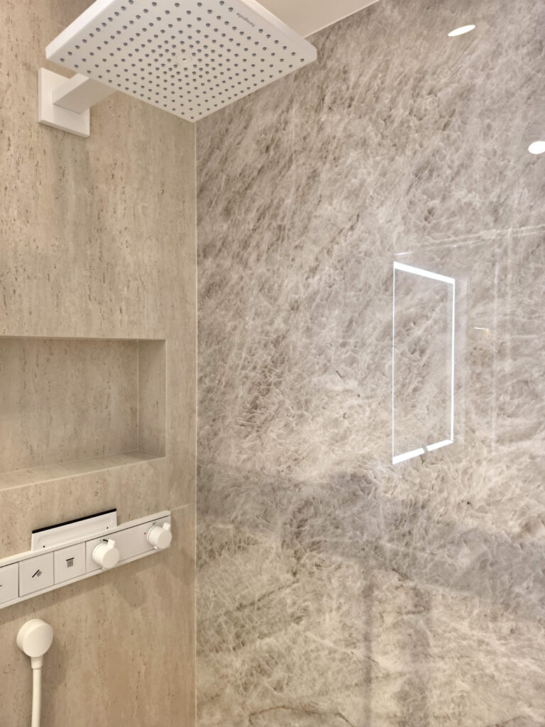 Ciel de pluie carré blanc Hansgrohe fixé au plafond et paroi de douche vitrée sur carrelage grand format effet pierre naturelle.