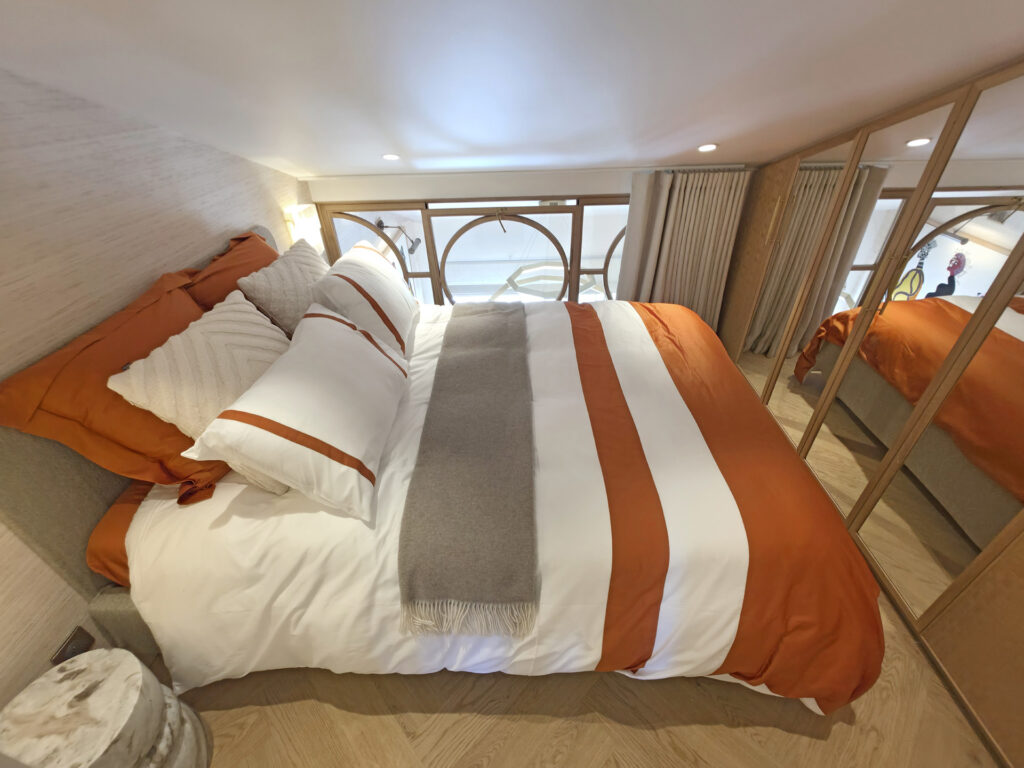 Chambre en mezzanine sous pente avec lit coffre terracotta, placards aux portes miroir et verrière ouvrante sur mesure donnant sur le salon.